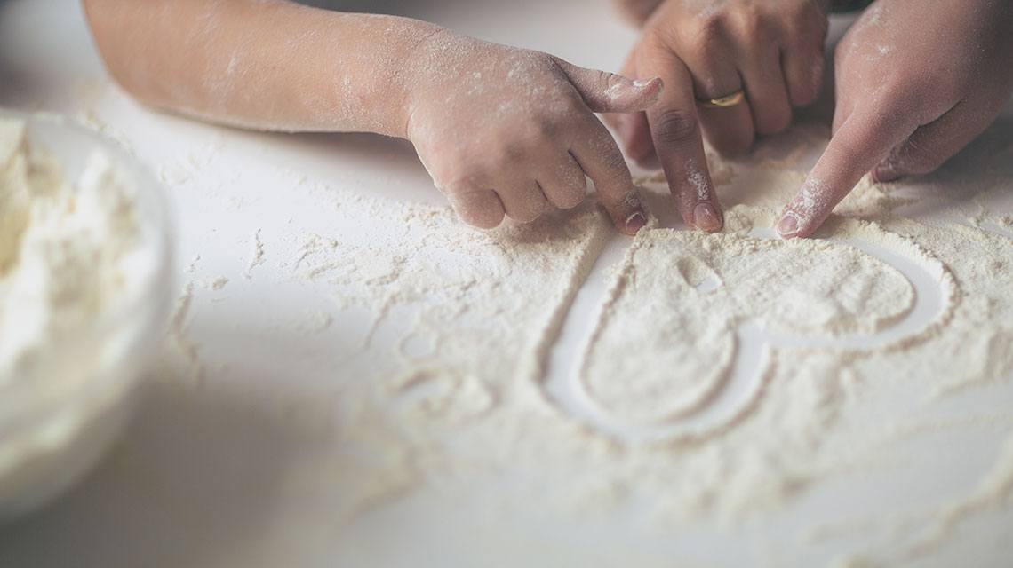 Two hands shaping a heart out of flour, that contains gluten