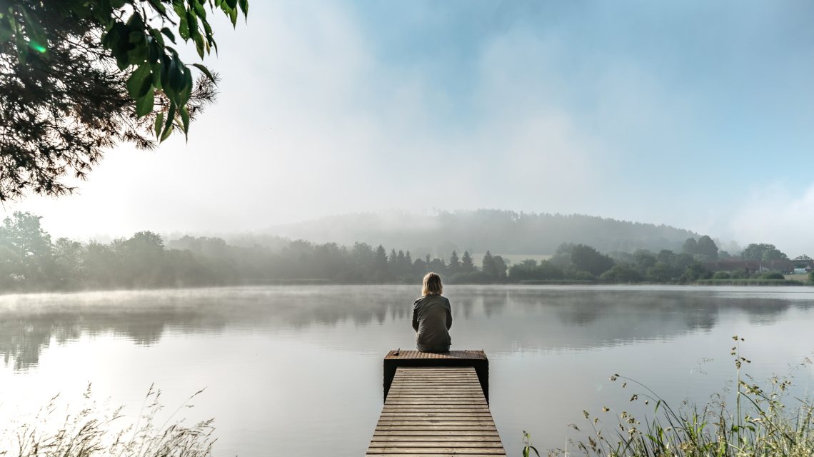 Mood picture for International Self-Care Day 2025, showing a women sitting by a lake